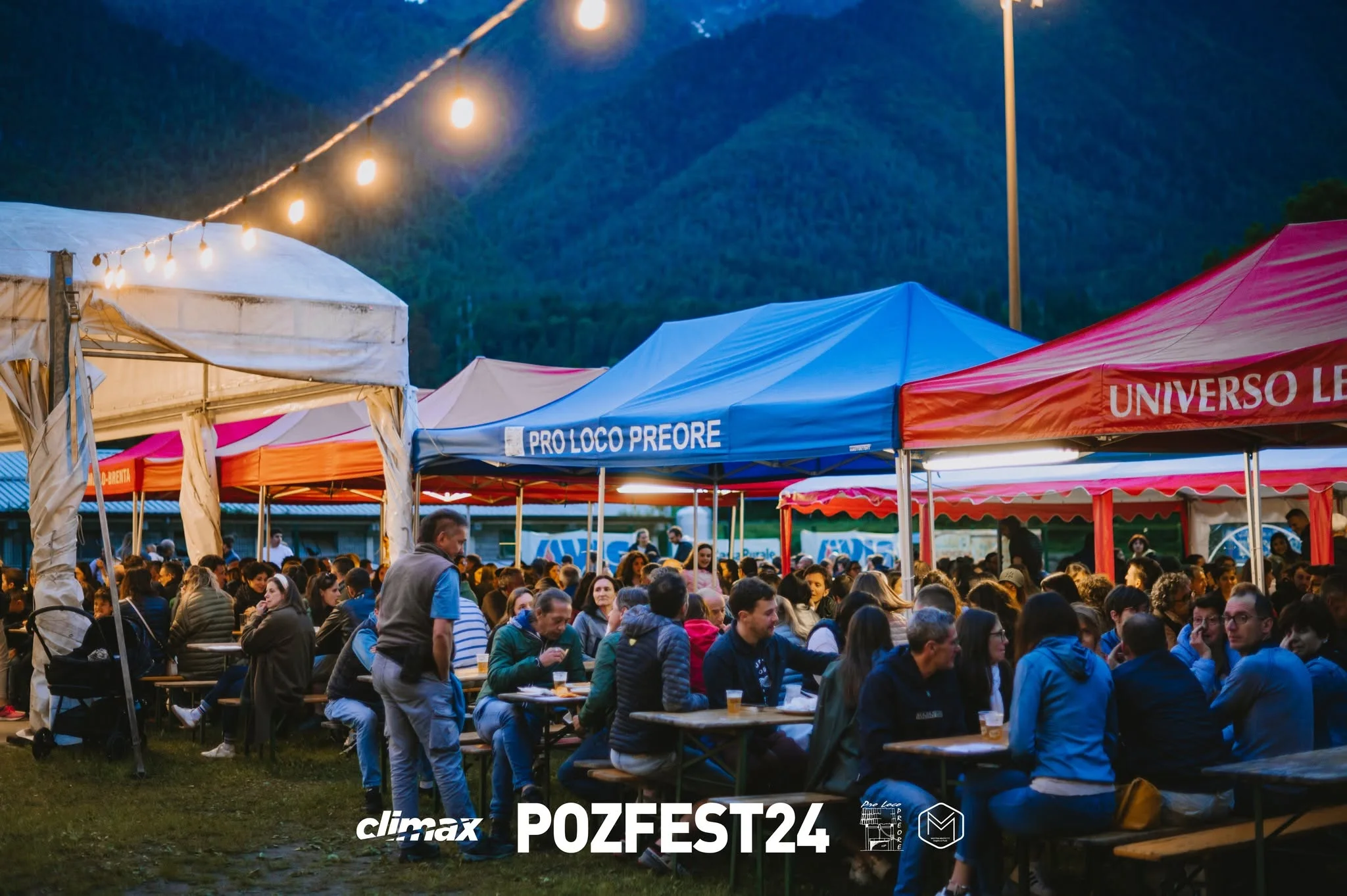 I tavoli della festa al tramonto tra i gazebo della Pro Loco e i filari di luci, con le montagne sullo sfondo