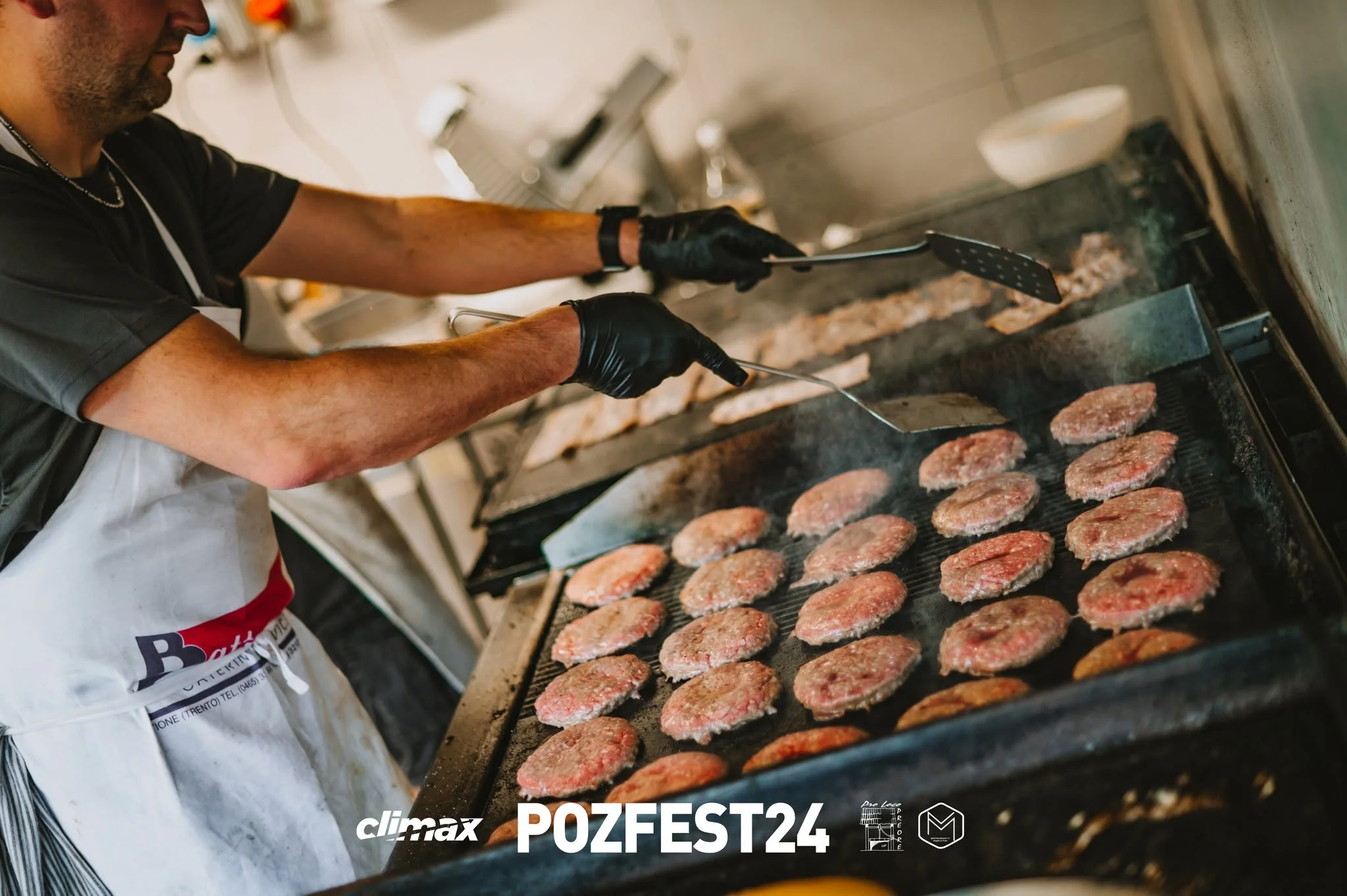 In cucina al POZFEST: un volontario alla griglia piena di hamburger